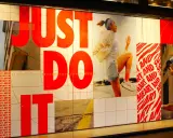 Slogan "Just Do It" in rosso su vetrina Nike, con atleti in corsa. Esempi di slogan motivazionali.