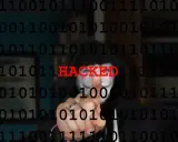 Persona con maschera anonima e codice binario sullo sfondo. La parola "HACKED" in rosso indica il significato di hackerato.