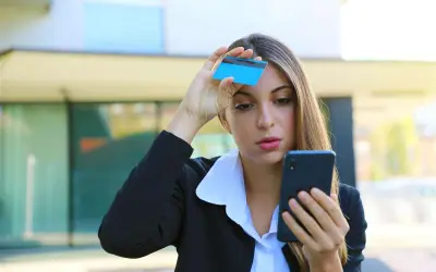 Donna preoccupata guarda il telefono con una carta in mano, temendo una carta clonata.