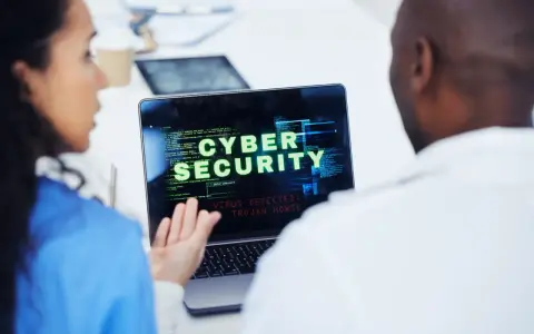Due professionisti analizzano un avviso di sicurezza informatica su un laptop: "VIRUS DETECTED: TROJAN HORSE".