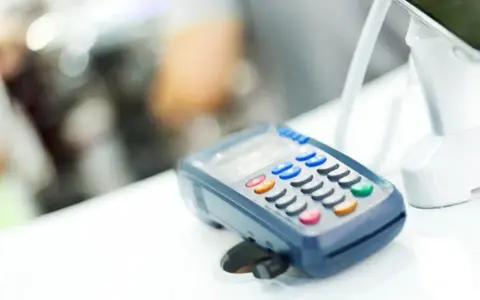 POS per chi non è obbligatorio. Un lettore di carte di credito su un bancone bianco, con uno schermo e tasti colorati.