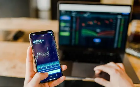 Mani che controllano grafici di Bitcoin su smartphone e laptop, un promemoria visivo delle potenziali truffe trading online.