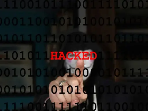 Persona con maschera anonima e codice binario sullo sfondo. La parola "HACKED" in rosso indica il significato di hackerato.