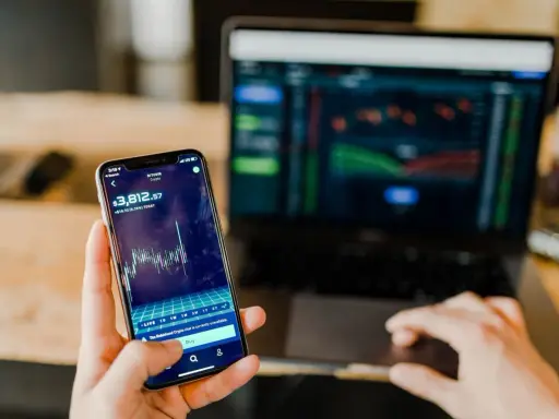 Mani che controllano grafici di Bitcoin su smartphone e laptop, un promemoria visivo delle potenziali truffe trading online.