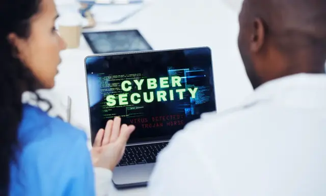 Due professionisti analizzano un avviso di sicurezza informatica su un laptop: "VIRUS DETECTED: TROJAN HORSE".